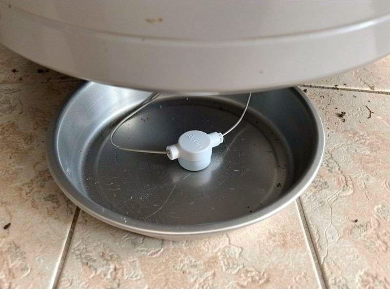 A water leak sensor with an external probe placed inside a metal drain pan under a water heater