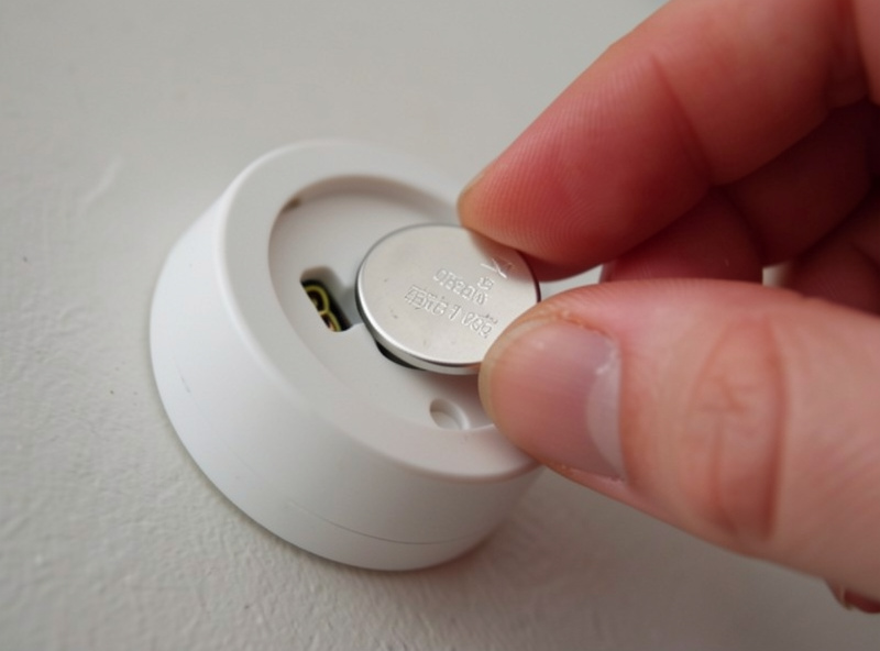 A hand replacing a coin cell battery in a small smart home contact sensor