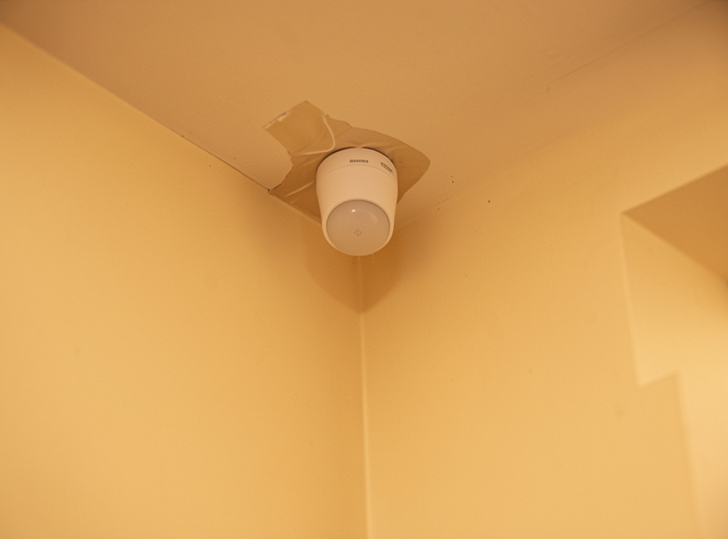 A small adhesive-mounted mmWave presence sensor in the corner of an apartment room