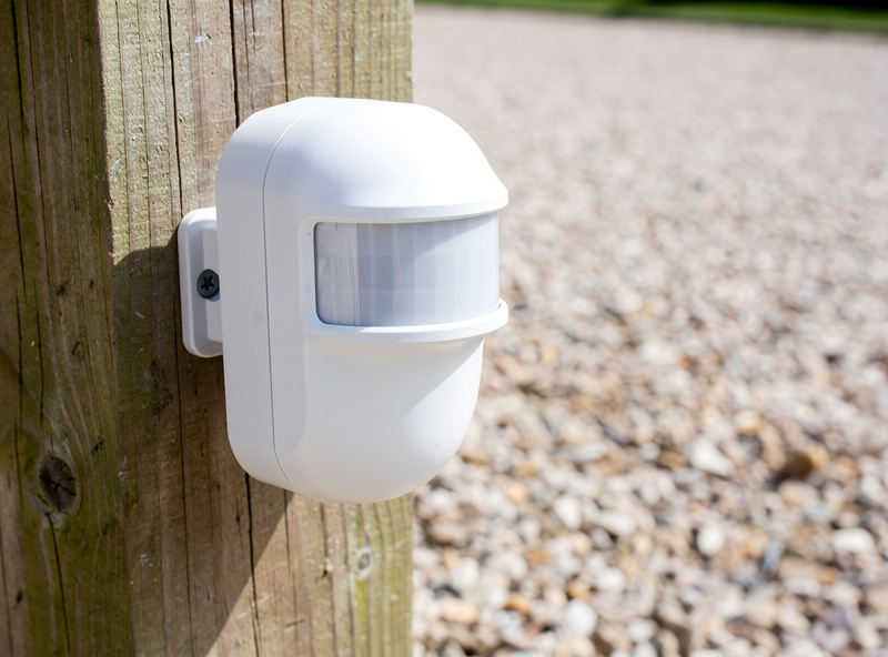 Weatherproof PIR driveway sensor mounted on a wooden post beside a gravel driveway
