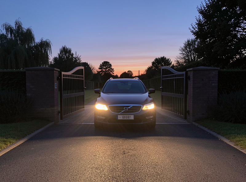 Car approaching an automated driveway gate at dusk with the gate beginning to open