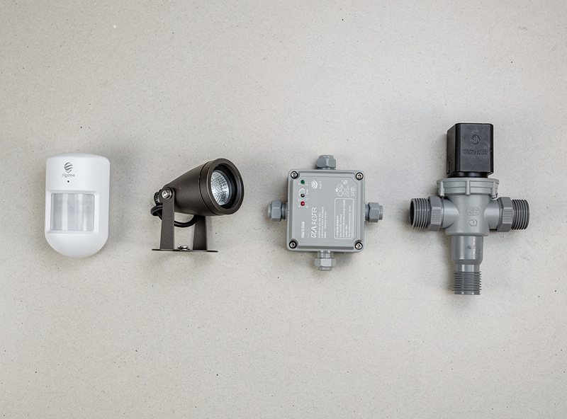 Outdoor smart home devices compared on a workbench: motion sensor, landscape light, relay, irrigation valve