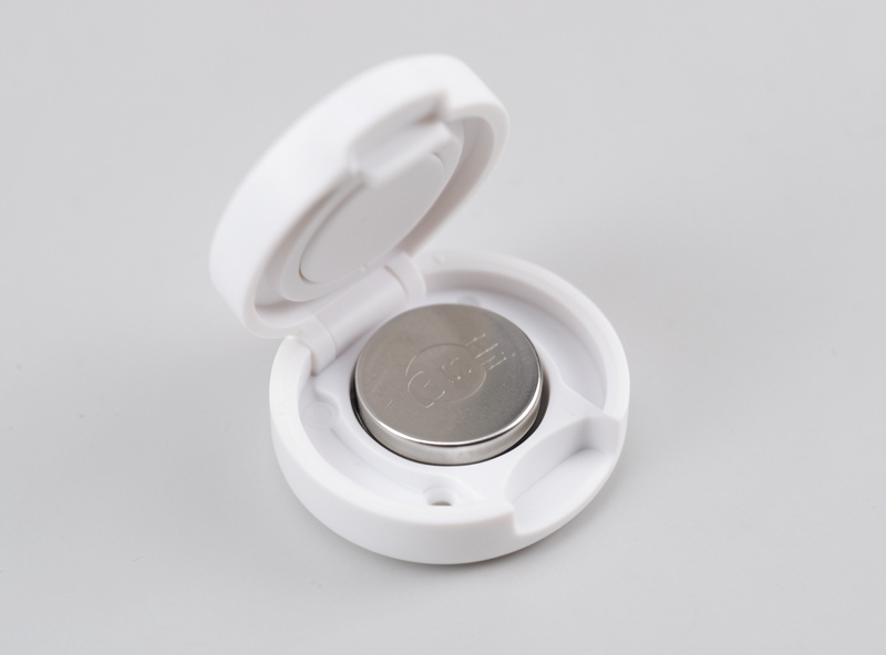 A small Zigbee contact sensor opened to show its coin cell battery on a workbench