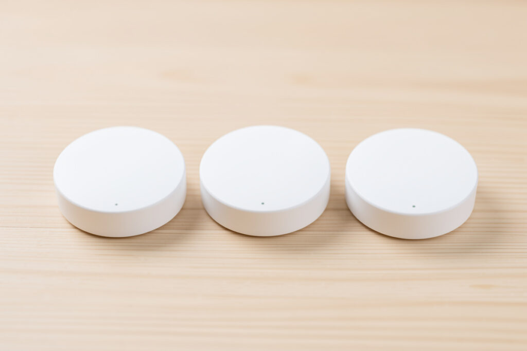 Three white disc-shaped mmWave presence sensors arranged in a row on a light wooden surface