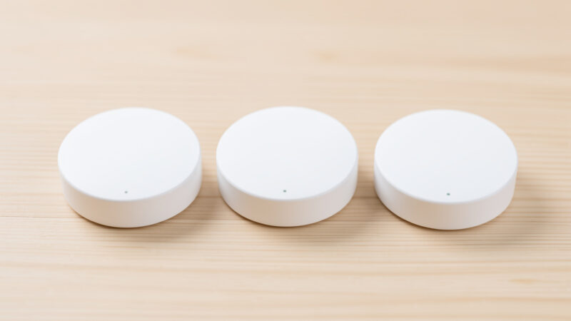 Three white disc-shaped mmWave presence sensors arranged in a row on a light wooden surface