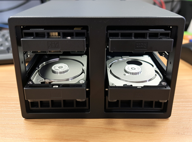 Network-attached storage NAS with two open drive bays holding hard drives on a desk