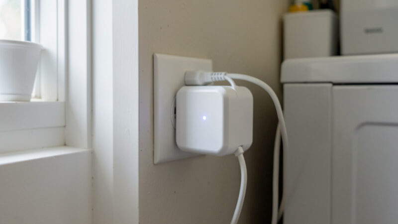 Energy-monitoring smart plug behind a washing machine in a home utility room