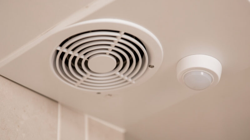Bathroom ceiling exhaust fan grille next to a small white disc presence sensor