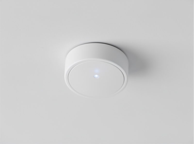 Close-up of a small round white mmWave presence sensor mounted on a ceiling